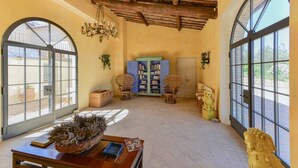 A spacious room with a high ceiling, large windows, a bookshelf, wicker chairs, and a decorative sculpture. - New Historic Tuscany Country House Retreat in a Vineyard Near Siena Villa Chiantissimo (Castelnuovo Berardenga)