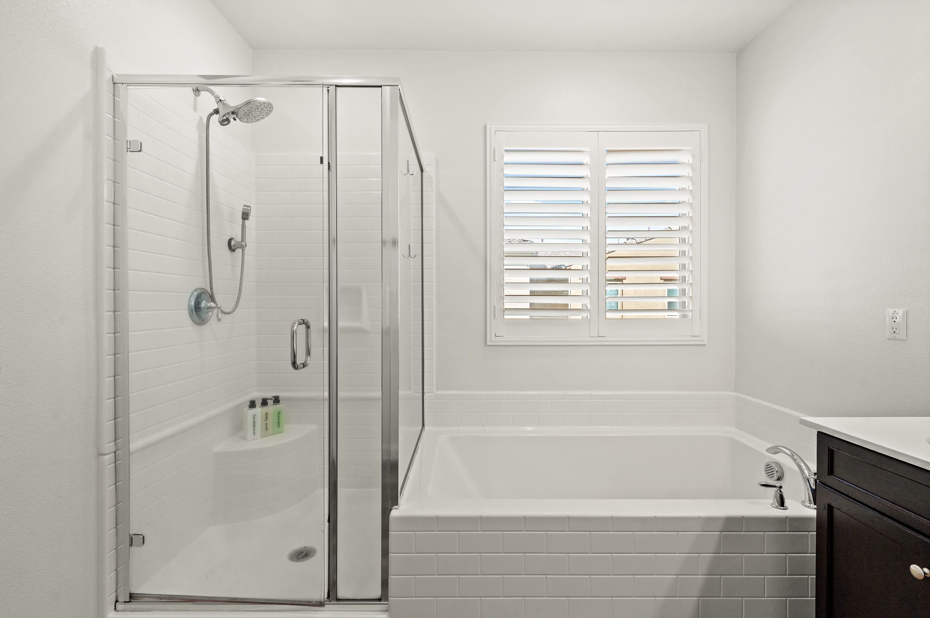 Un baño con ducha de vidrio, bañera y ventana con persianas.