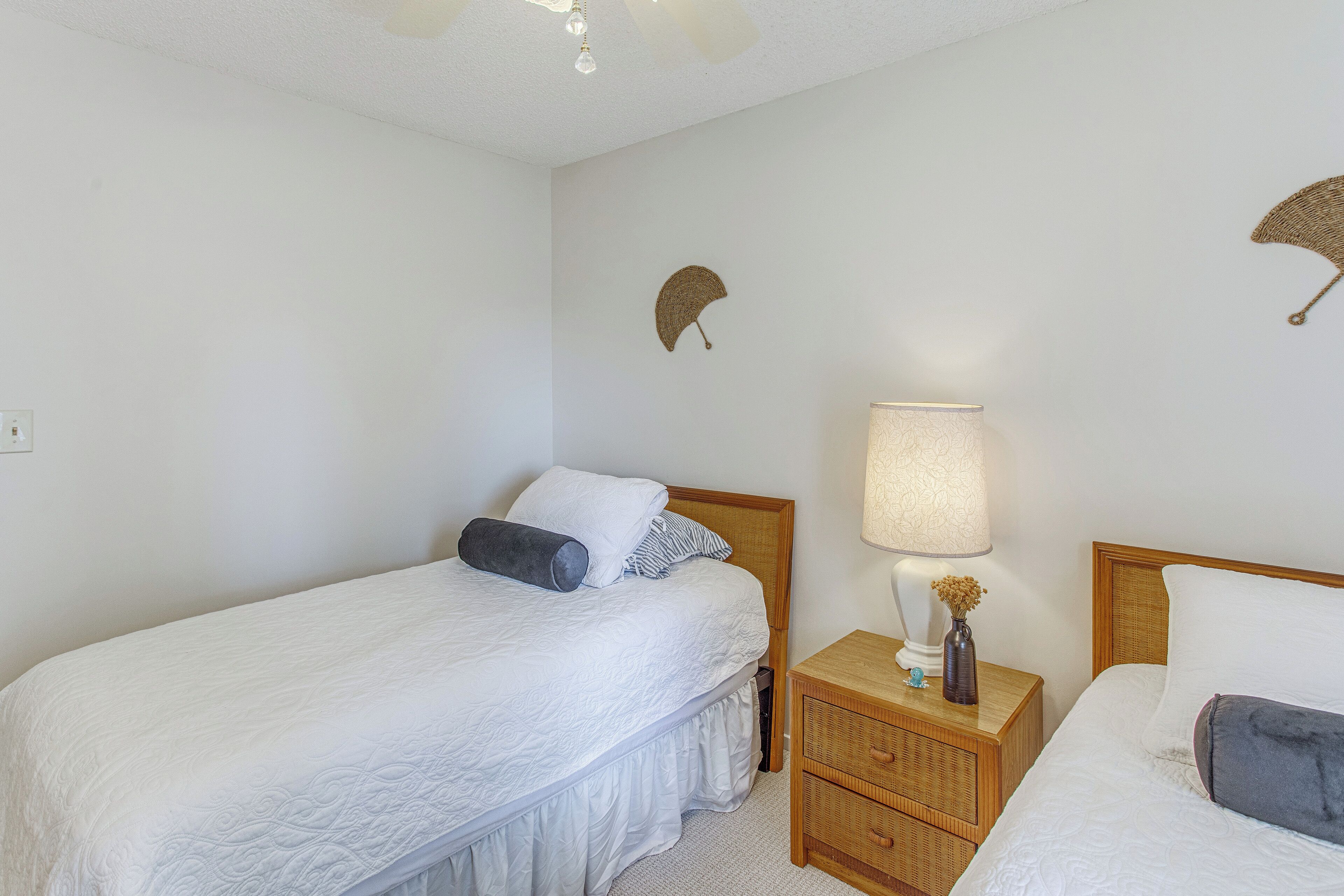 Une chambre avec deux lits simples, une table de chevet avec une lampe et des œuvres d’art décoratives au mur.