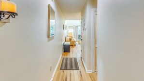 Un pasillo con suelo de madera, un tapiz, un banco y una puerta que da a otra habitación.