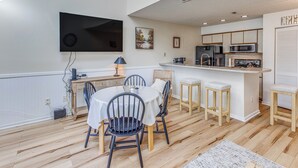 Una cocina moderna con una isla central, un comedor con una mesa redonda y sillas, y un televisor de pantalla plana montado en la pared.