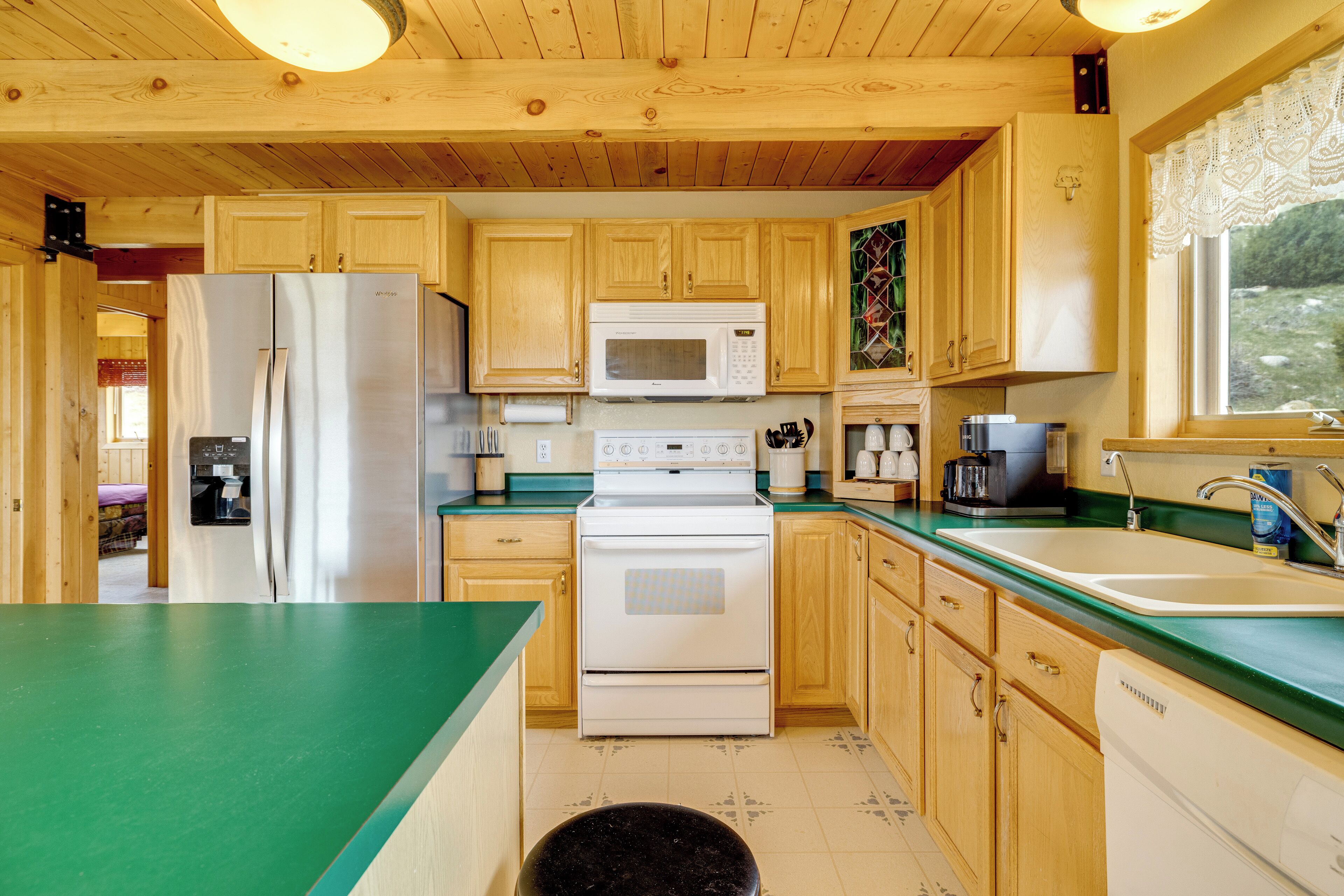 A kitchen with wooden cabinets, a stainless steel refrigerator, a white microwave, a stove, and a sink.