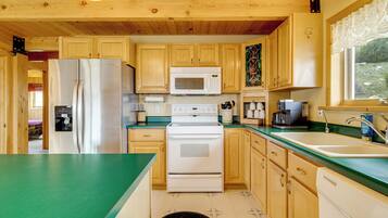 A kitchen with wooden cabinets, a stainless steel refrigerator, a white microwave, a stove, and a sink.