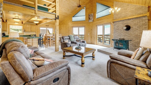 A spacious living area with wooden flooring, leather sofas, a wooden coffee table, and a kitchen in the background. - Walk to Sinks Canyon State Park: Spacious Home! (Lander)