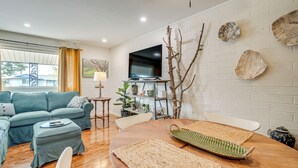 Una sala moderna con sofá, mesa de centro, televisor montado en la pared y elementos decorativos como ramas y platos.