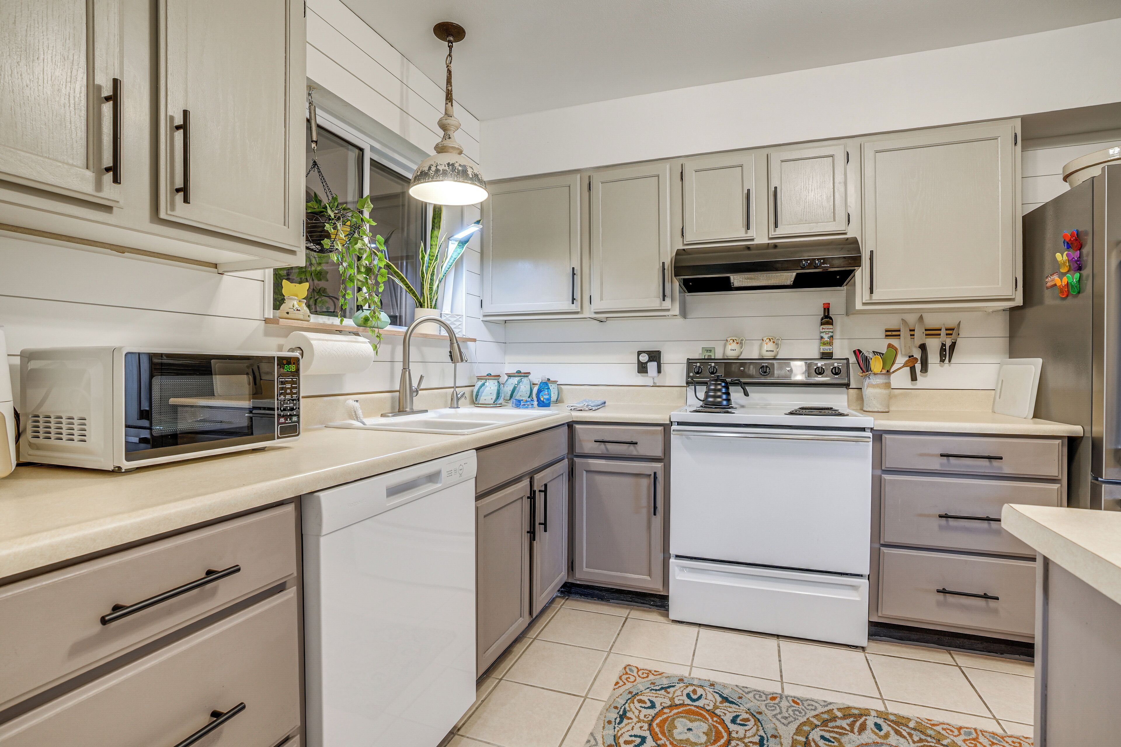 A modern kitchen with white cabinets, stainless steel appliances, and a patterned rug.