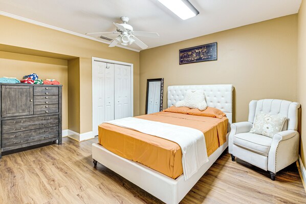 Un dormitorio con cama, una silla, tocador y ventilador de techo.