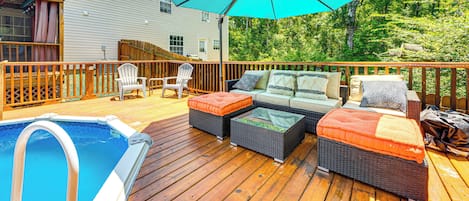 A wooden deck with a pool, outdoor furniture, and a large umbrella.