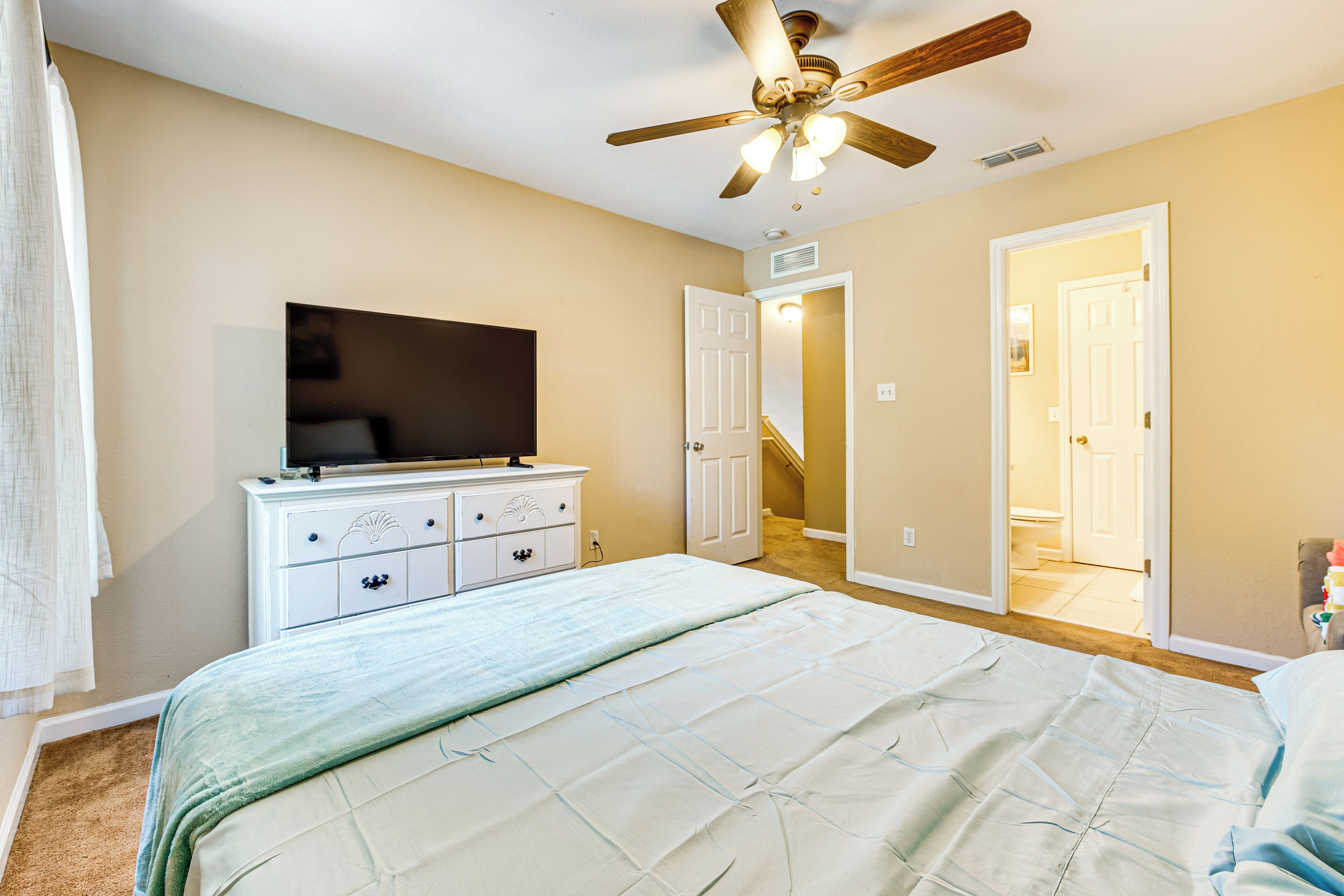A bedroom with a bed, a dresser, a ceiling fan, and a television.