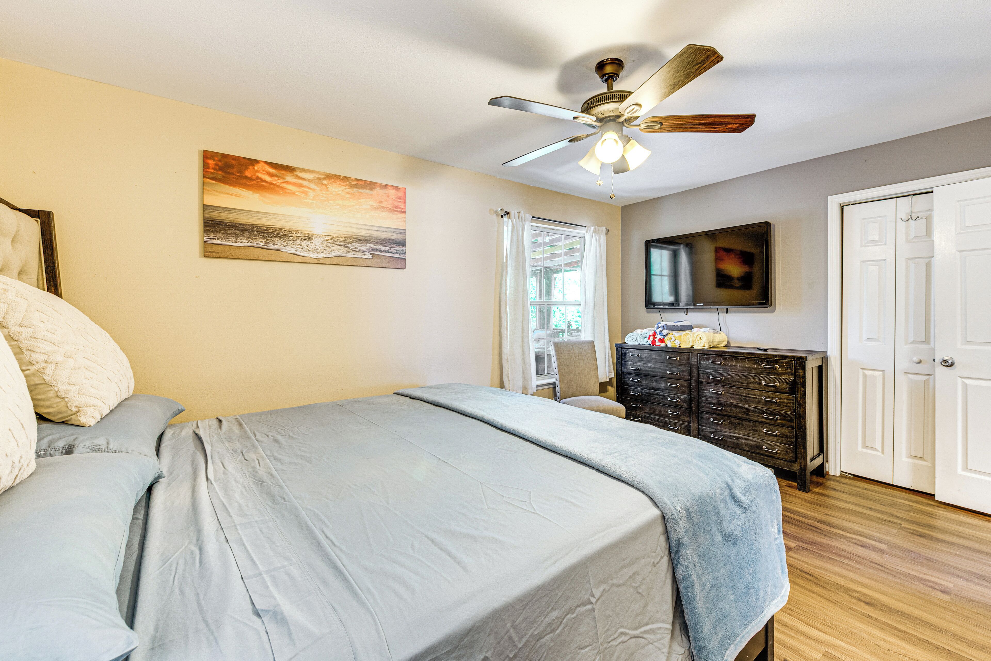 A bedroom with a bed, a ceiling fan, a dresser, a television, and a door.