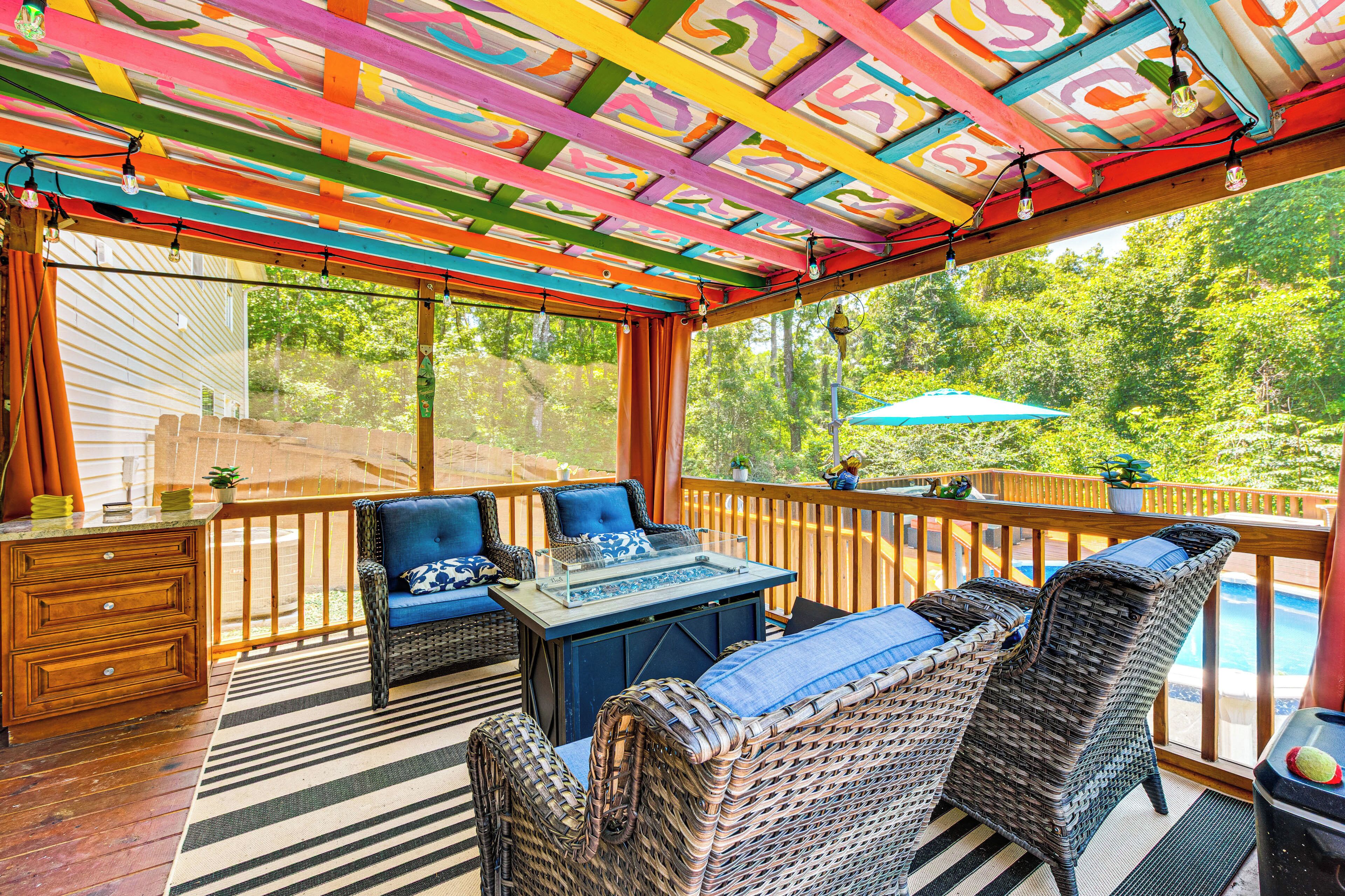 A covered outdoor seating area with wicker furniture, a glass-top table, and a view of a swimming pool.