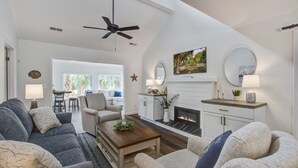 Ein geräumiges Wohnzimmer mit Kamin, bequemen Sitzgelegenheiten und einem Deckenventilator.