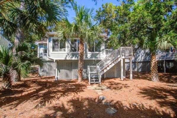A two-story house with a covered porch, a staircase, and a fenced yard with palm trees.