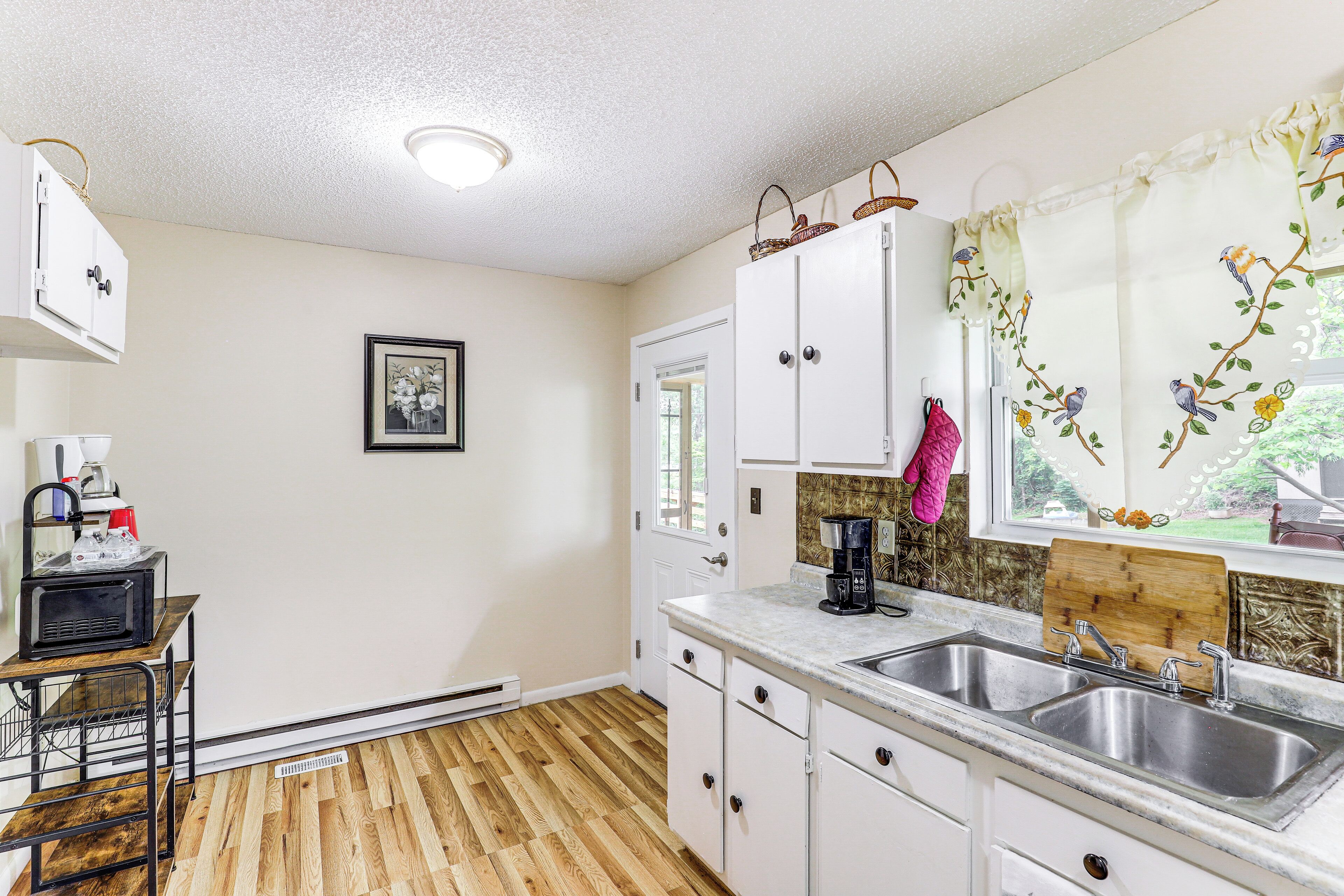 A kitchen with white cabinets, a double sink, and a wooden floor.