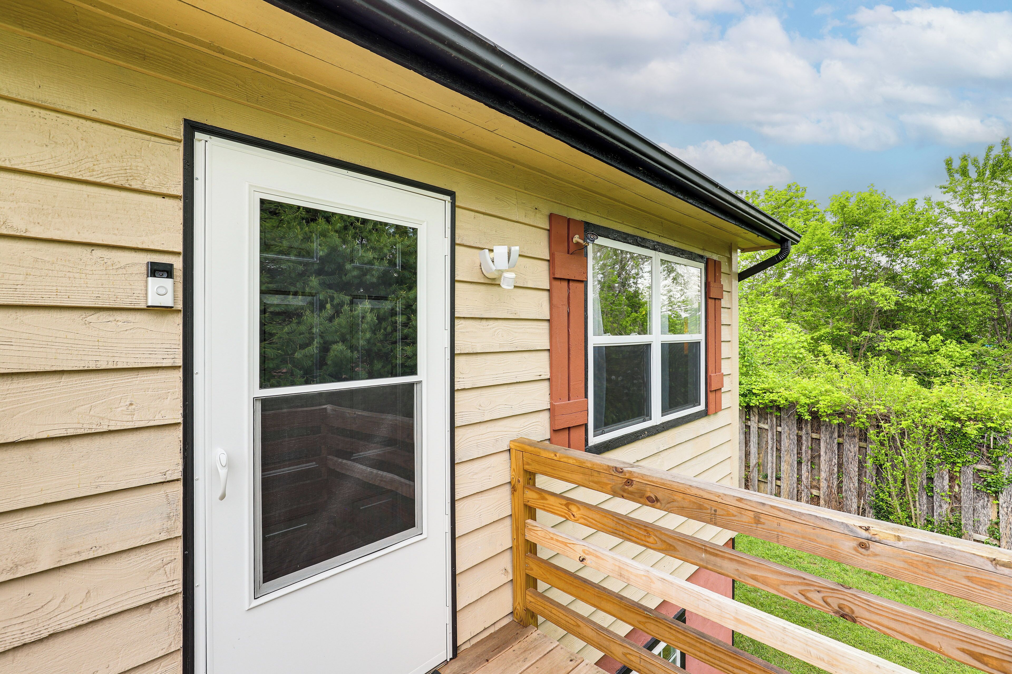 A wooden deck with a bench, a house with beige siding, and a white door.