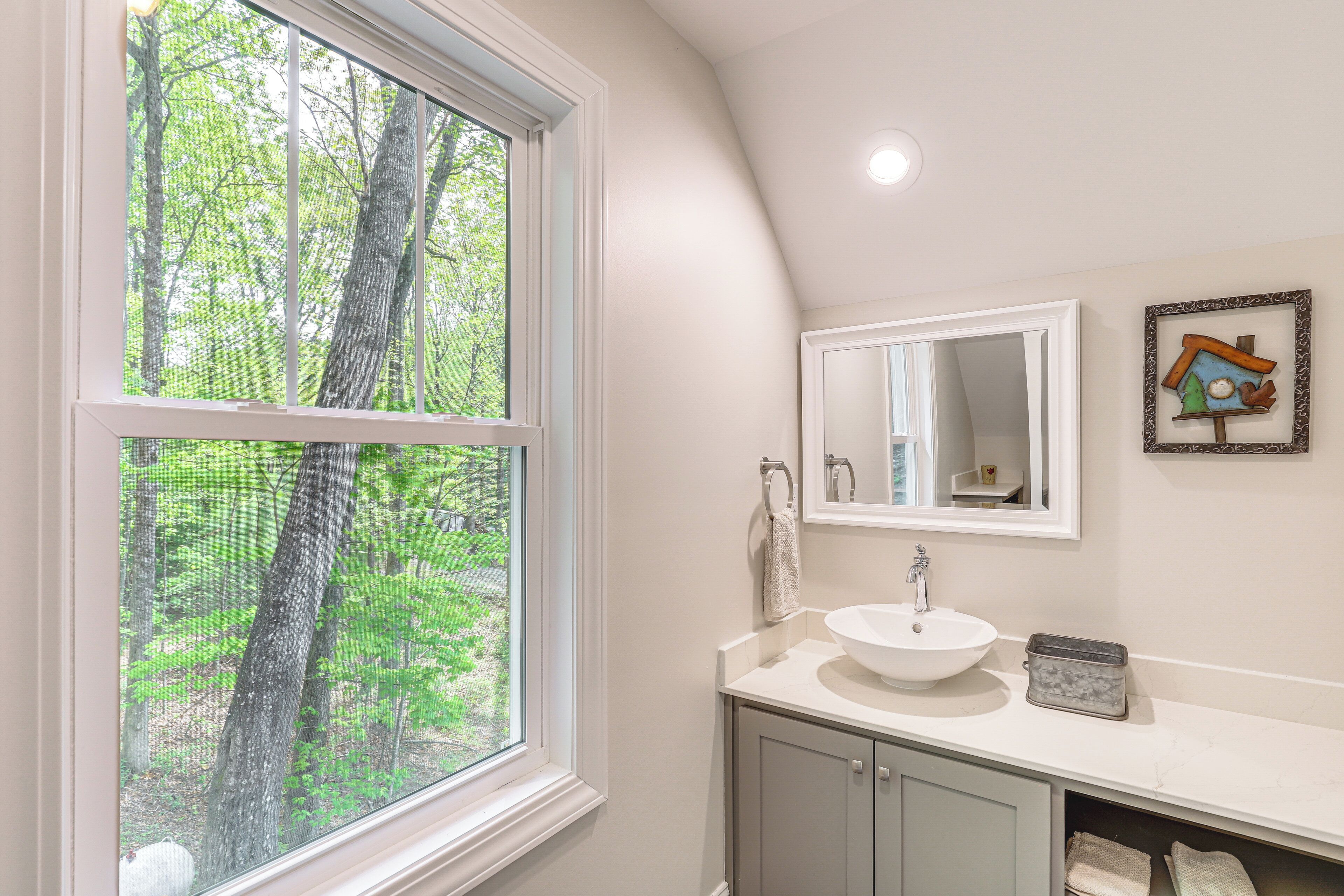 A bathroom with a large window, a sink, a mirror, and a cabinet.