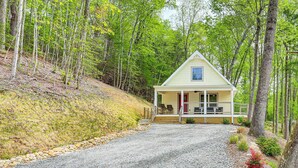 Une petite cabane à un seul étage, dotée d’un porche et d’une allée en gravier, et entourée d’arbres.