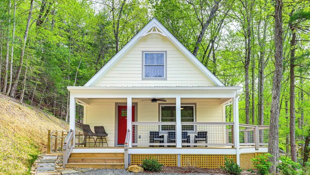 Une cabane de plain-pied avec une véranda, une porte rouge et une petite fenêtre.