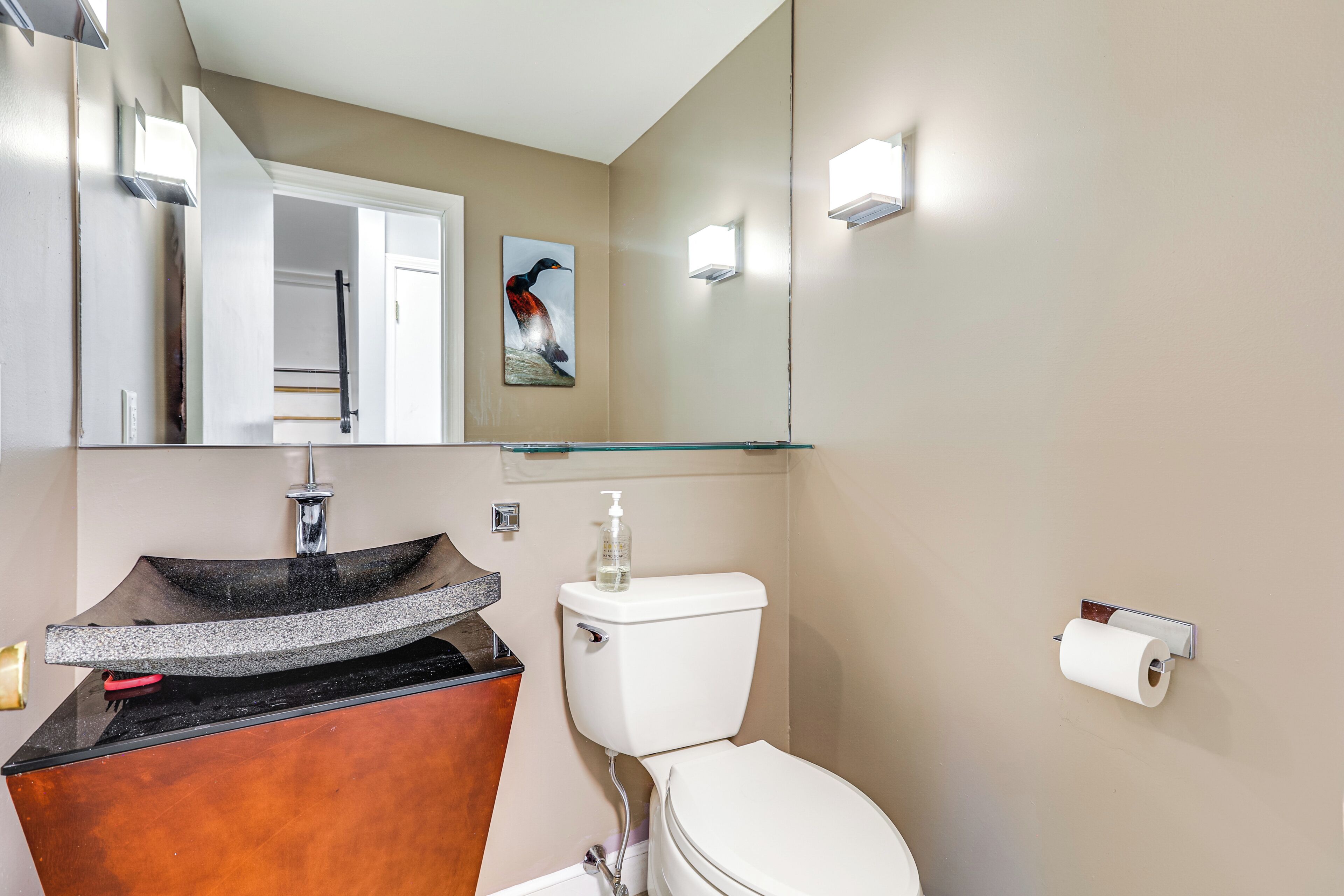 Un bany amb un lavabo modern, vàter i una prestatgeria de vidre sobre el lavabo.