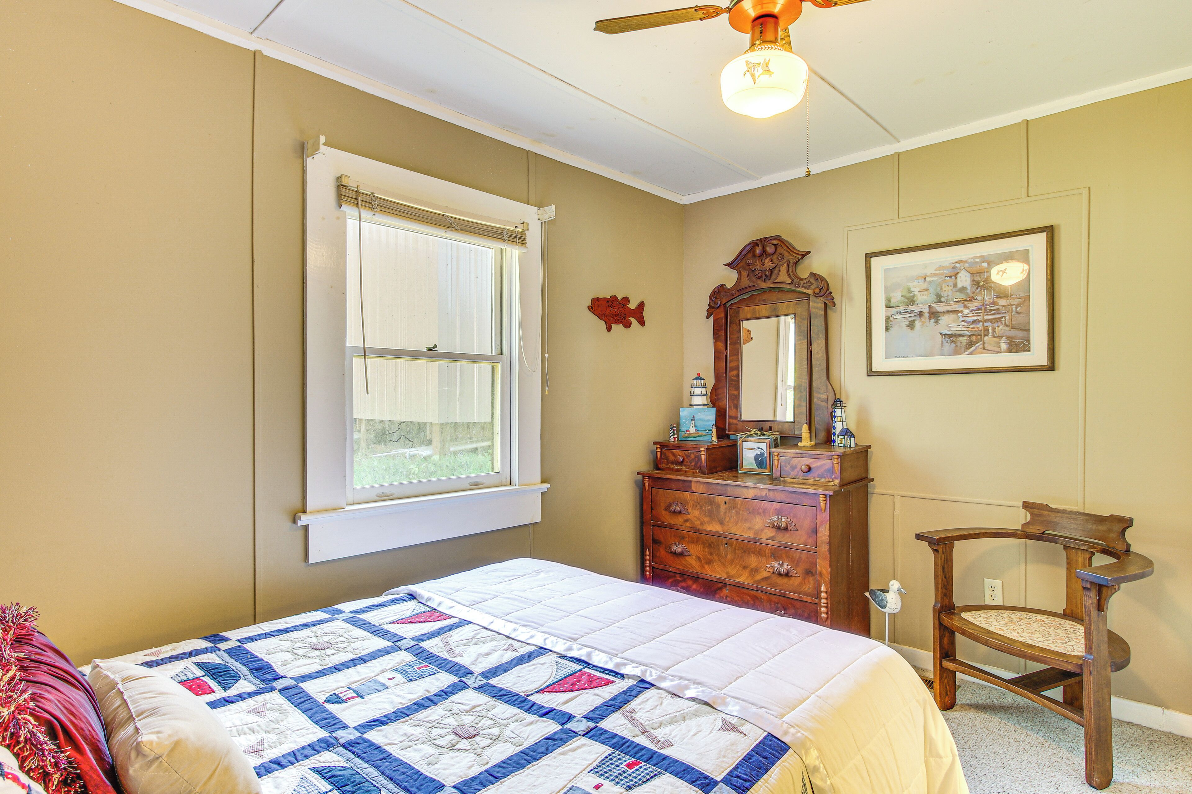 A bedroom with a bed, a dresser, a chair, a window, a ceiling fan, and a framed picture on the wall.