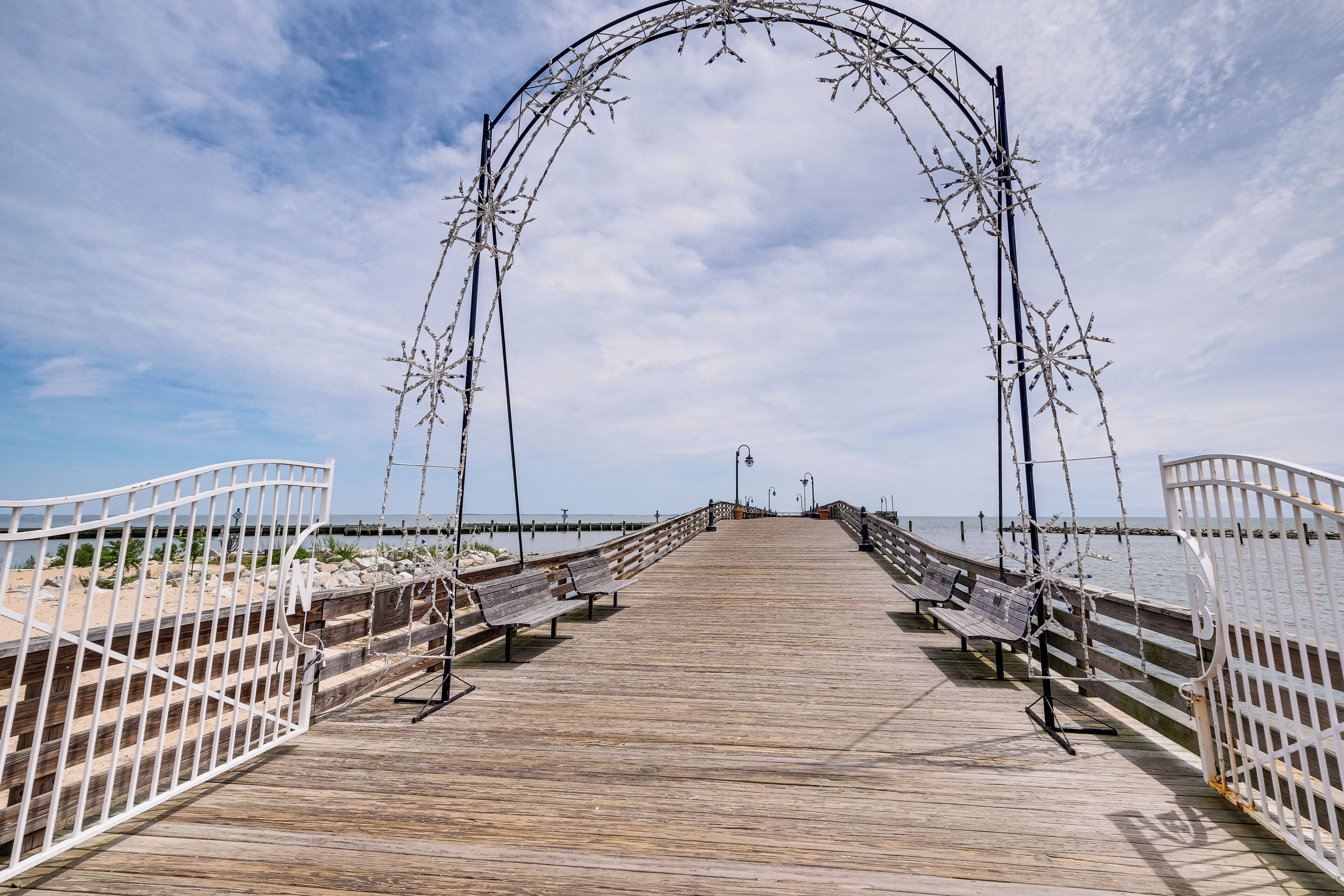 A wooden pier with benches and railings, leading to a body of water.