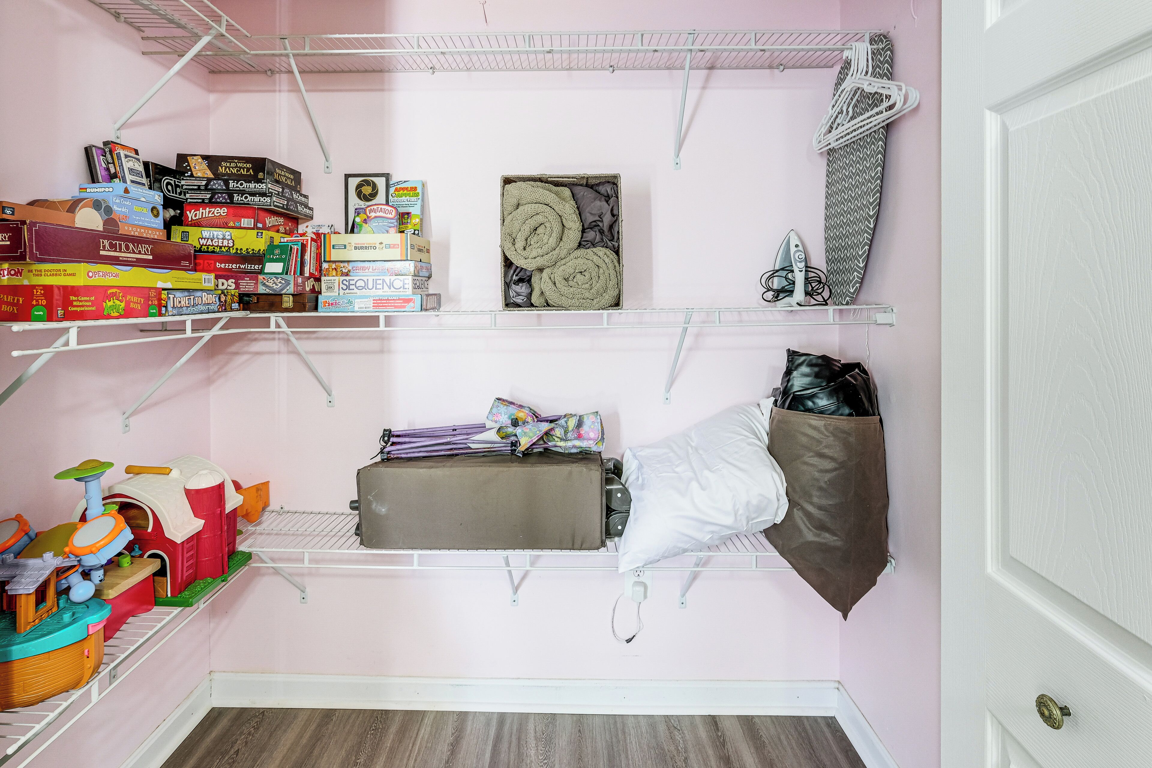 A pink room with a bed, shelves with books and games, and a suitcase.