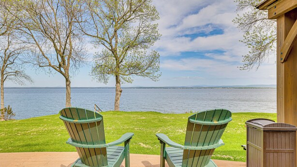 Dos sillas Adirondack mirando un lago, con una terraza de madera y un cobertizo.
