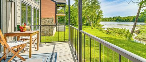 A balcony with a view of a river, a wooden table with chairs, and a stone wall.