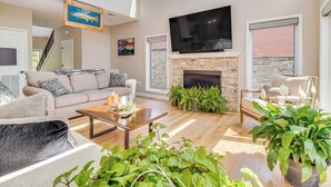 Un salón amplio con chimenea, un televisor grande montado encima y un área de estar cómoda con sofá y sillones.