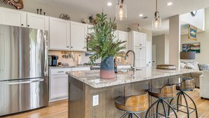 Una cocina moderna con una isla grande, electrodomésticos de acero inoxidable y taburetes de bar de madera.