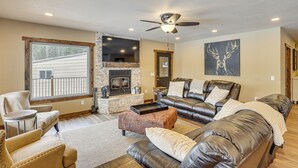 A spacious living room with leather sofas, a fireplace, and a large window overlooking a deck. - Black Hills Vacation Lodge: New Home! Just Opened! (Newcastle)