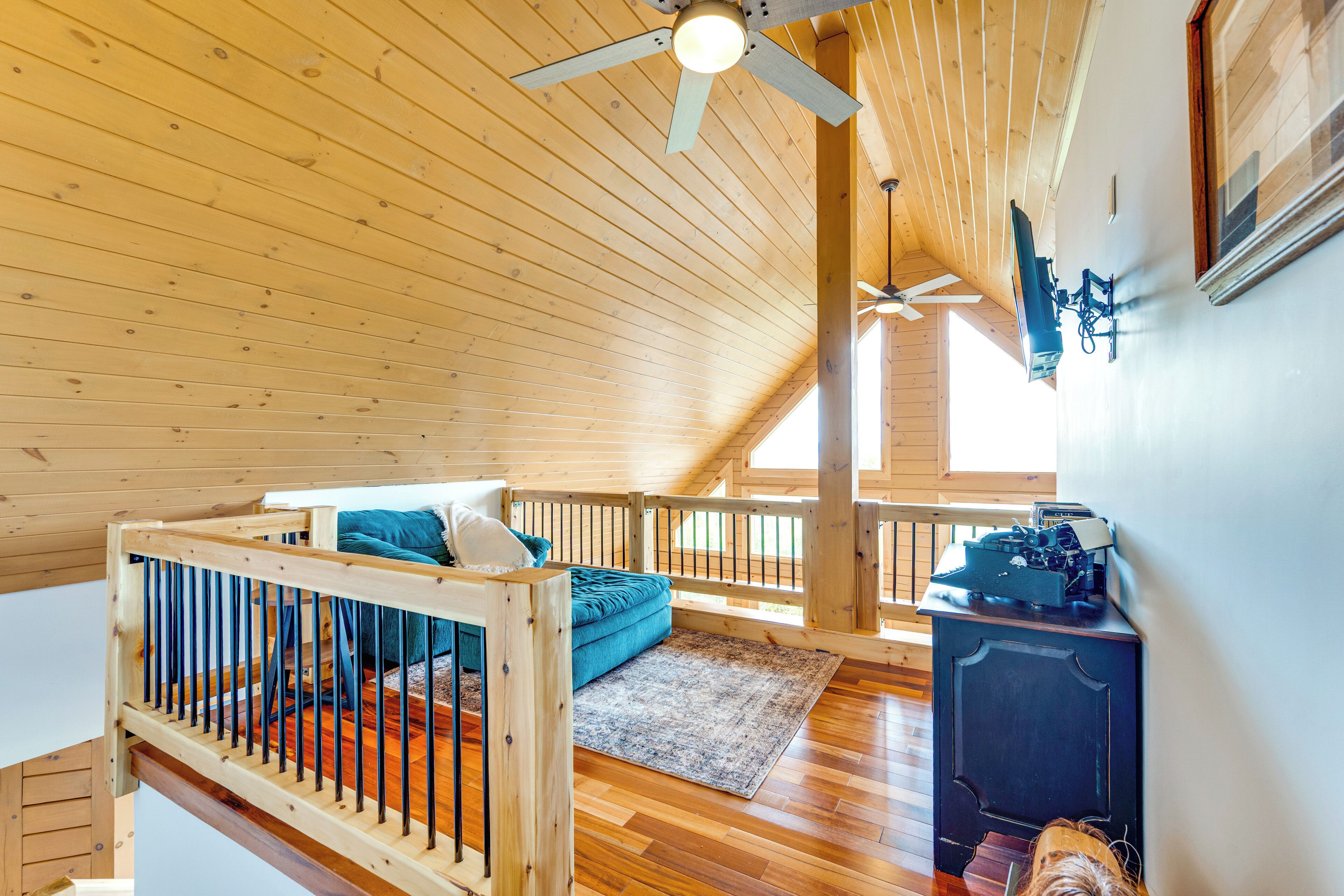 A wooden interior with a loft bed, a desk, and a ceiling fan.