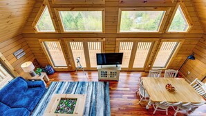 A cozy cabin with a large wooden ceiling, multiple windows offering views of the outdoors, a dining area with a table and chairs, and a living room with a sofa and a coffee table. - Mtn-view Deck: Scenic Conway Log Cabin! (Conway)