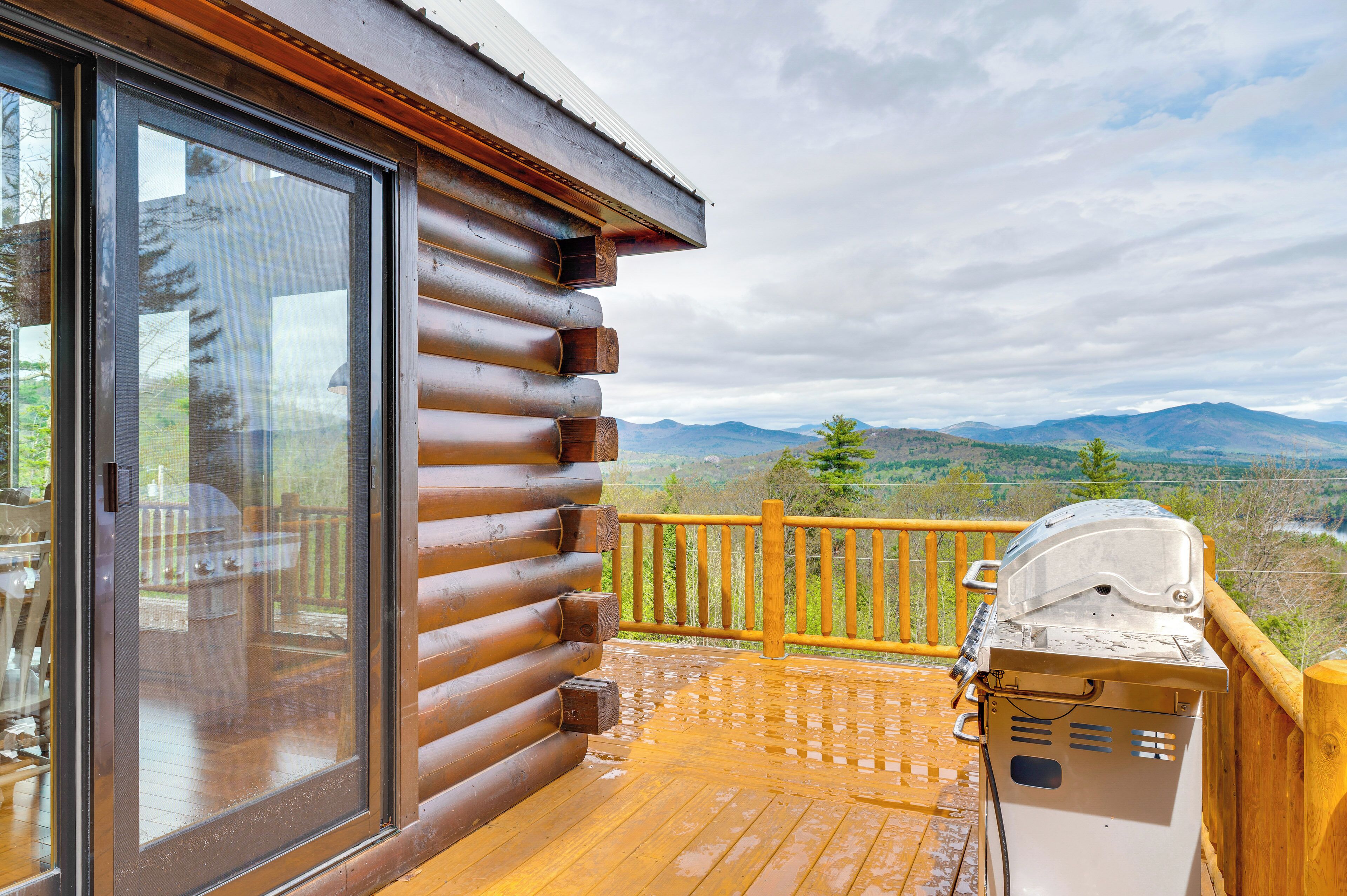 A wooden deck with a grill and a glass door leading to a deck area with a mountain view.