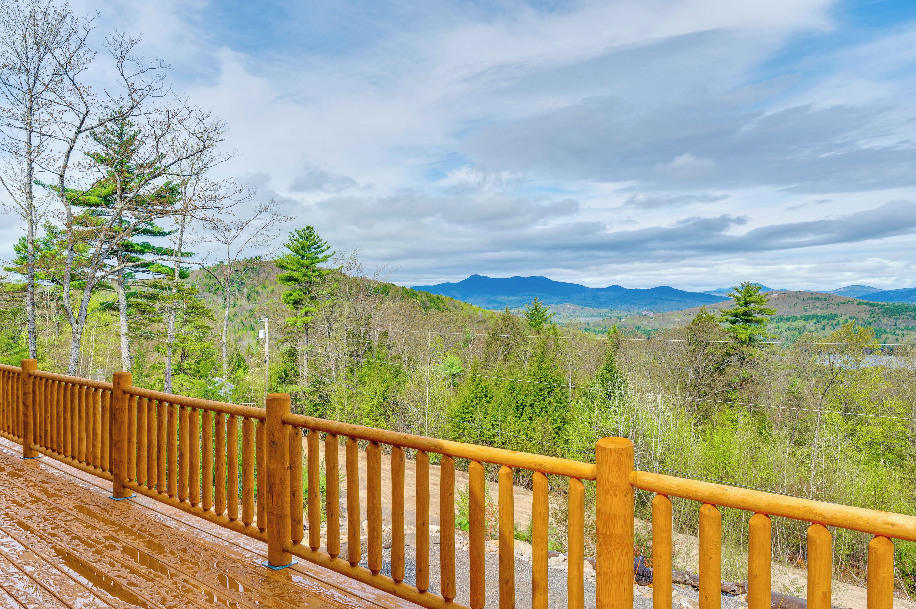 Una terraza de madera con barandilla que da a un paisaje forestal con montañas al fondo.