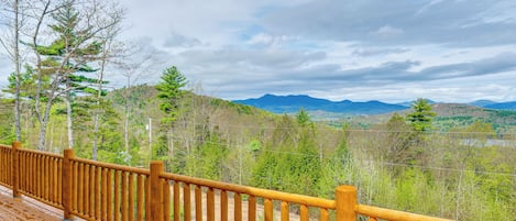 Una terraza de madera con barandilla que da a un paisaje forestal con montañas al fondo.