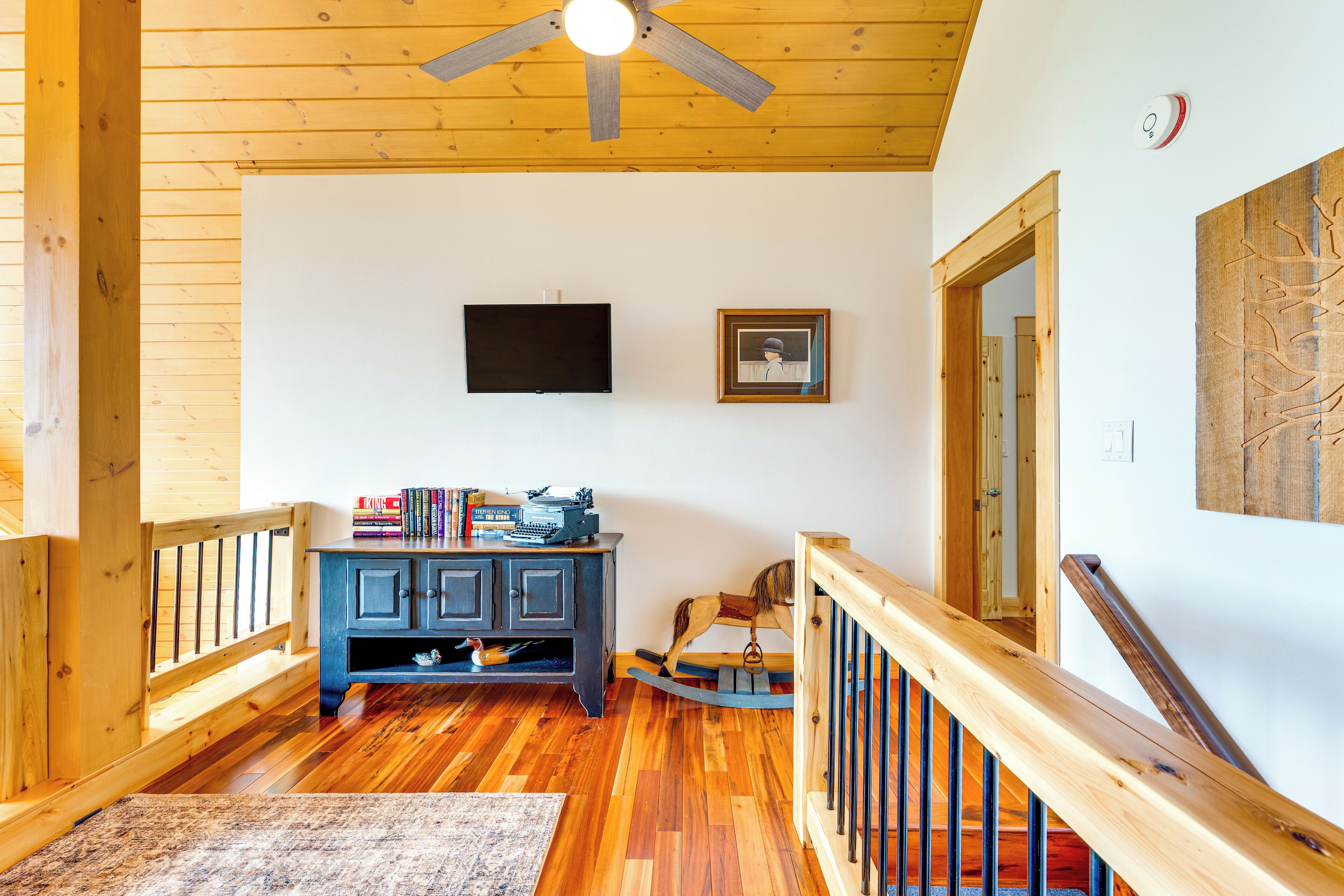 A wooden-floored hallway with a ceiling fan, a mounted TV, and a framed picture on the wall.