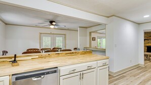 A kitchen with a wooden countertop, white cabinets, a dishwasher, and a ceiling fan.