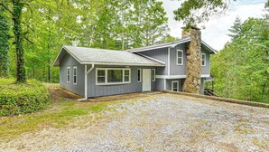 A two-story house with a stone chimney, a covered porch, and a gravel driveway.