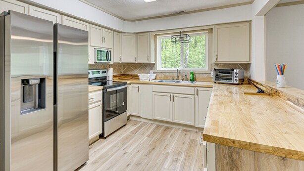 A modern kitchen with stainless steel appliances, wooden countertops, and a large window providing natural light.