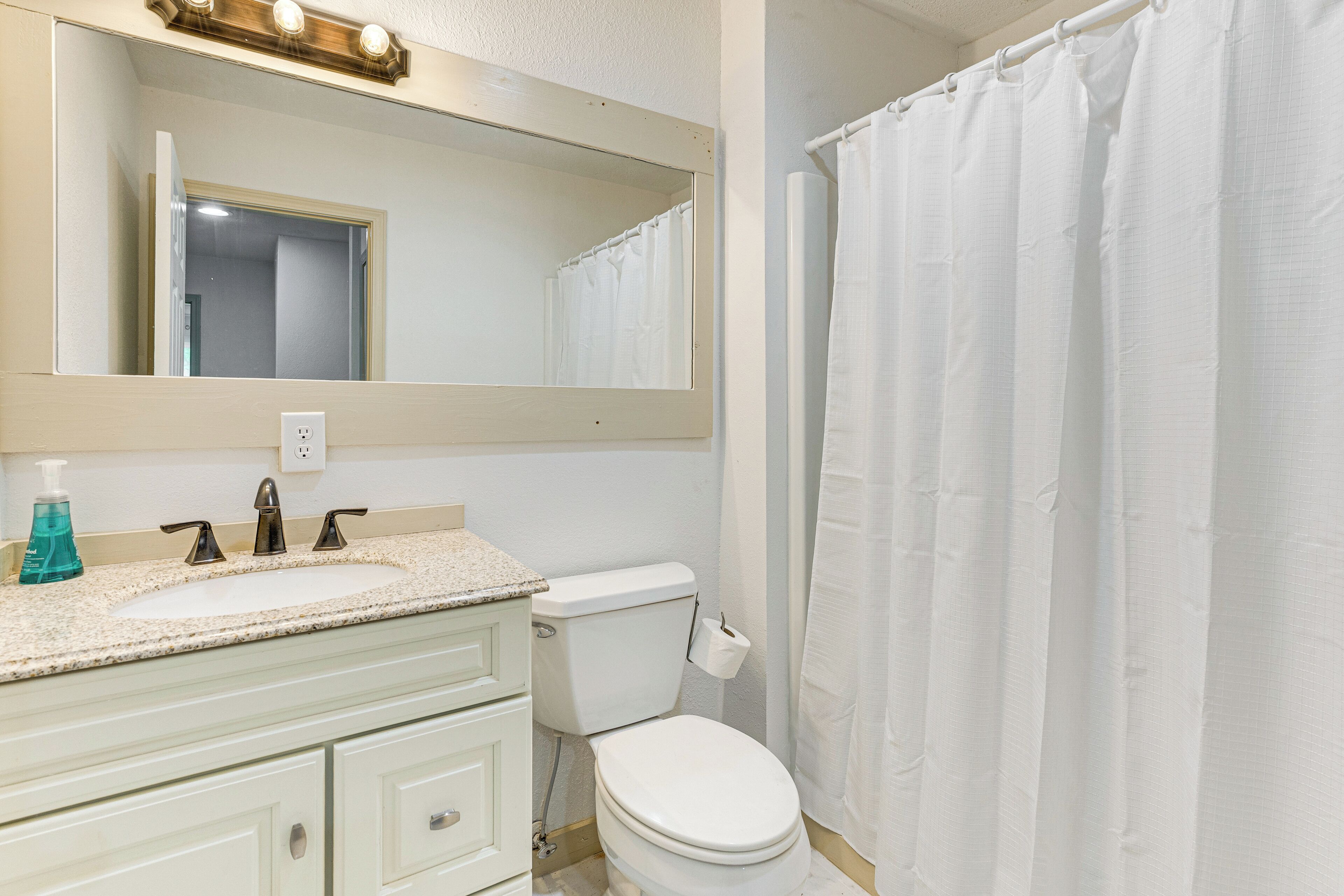 A bathroom with a sink, mirror, toilet, and shower curtain.