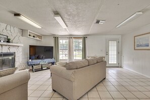 A living room with a sofa, a flat-screen TV, a fireplace, and a large window with curtains. - Homosassa Getaway w/ Pool & Refreshed Lanai (Homosassa)