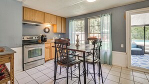 A kitchen with wooden cabinets, a stainless steel oven, a dining table with chairs, and a large window with curtains. - Homosassa Getaway w/ Pool & Refreshed Lanai (Homosassa)