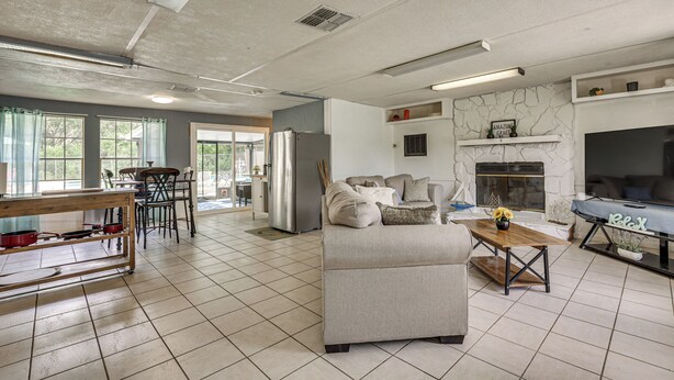A spacious living area with a sofa, a coffee table, a fireplace, and a kitchen area with a refrigerator and dining table. - Homosassa Getaway w/ Pool & Refreshed Lanai (Homosassa)