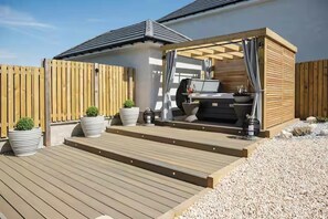 A wooden deck with a grill area, potted plants, and a pergola structure. - Stylish House in Perth-hot Tub-garden-sleeps 6 (Perth)