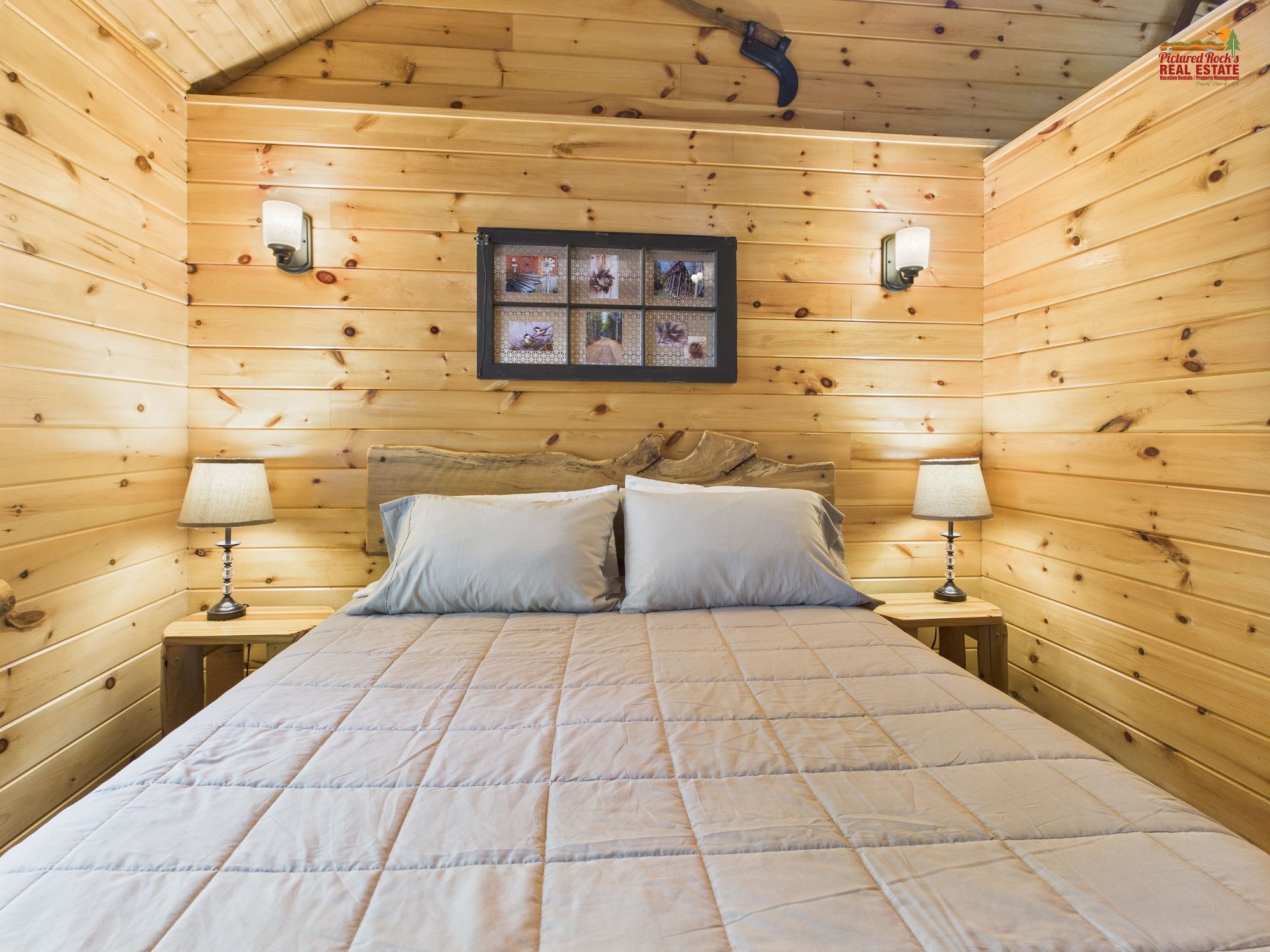 A wooden cabin bedroom with a bed, two bedside lamps, a framed photo collage, and a rustic headboard.