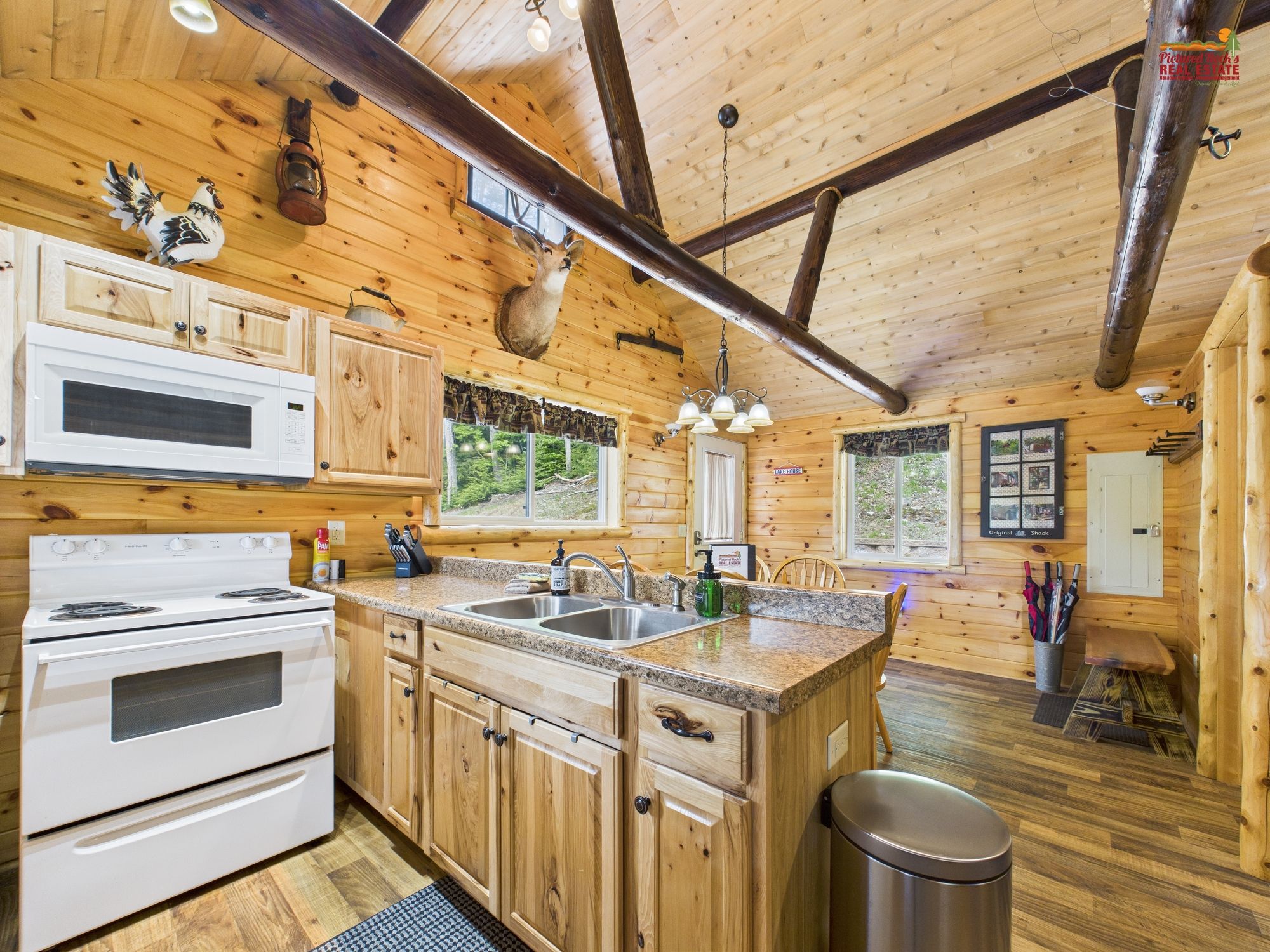 A wooden cabin interior with a kitchen featuring a stove, microwave, and sink.