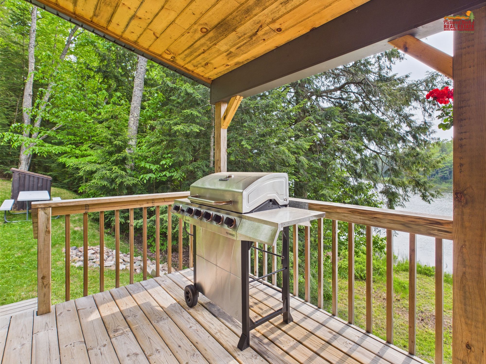 A wooden deck with a barbecue grill, overlooking a lake with trees.