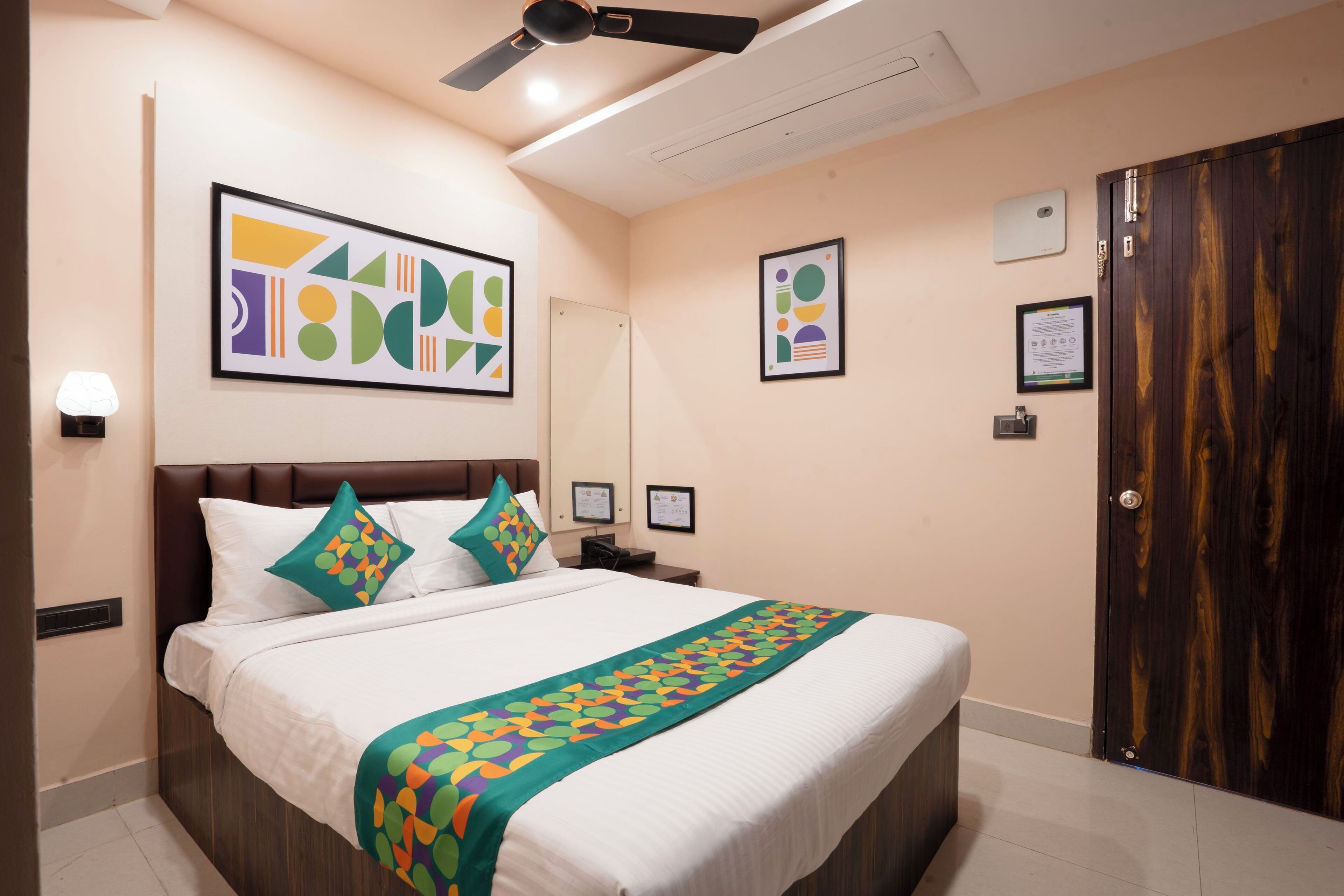 A hotel room with a large bed, a ceiling fan, a wooden wardrobe, and artwork on the walls.