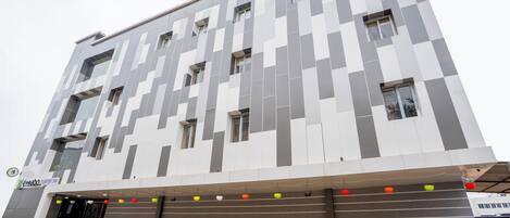 En moderne bygning med en geometrisk facade, mange vinduer og en trappe, der fører til indgangen.